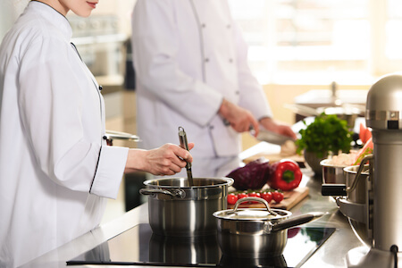 Cuisinier qui coupe des légumes et cuisinière brassant une soupe avec une louche