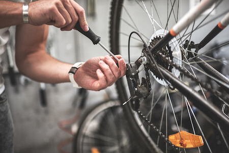 Mains d'un jeune homme tenant un tournevis pour réparer la chaîne d'une roue de vélo